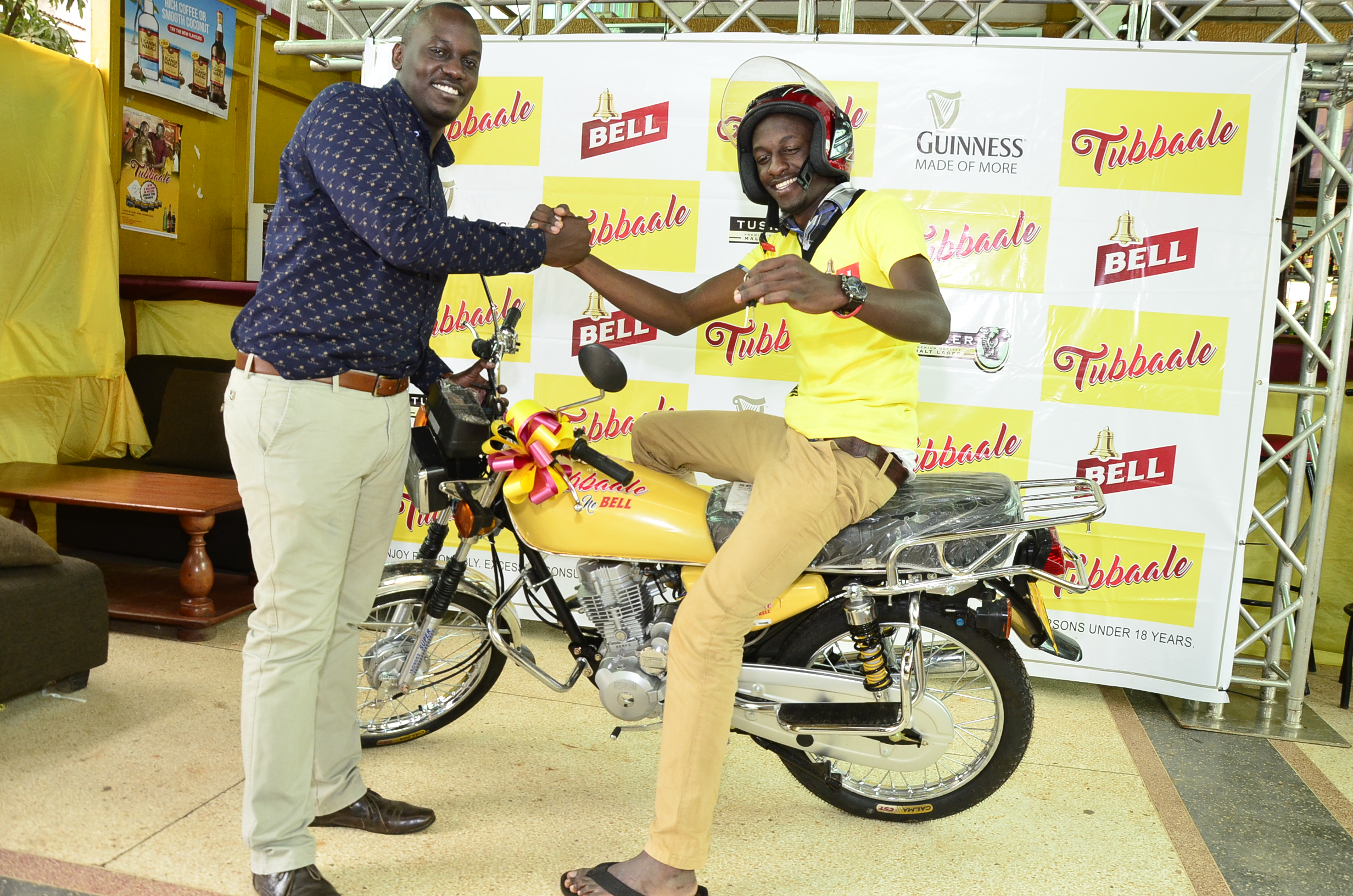 (L-R) Brian Seruyiggo, Customer Marketing Manager-Bell Lager congratulates Muwanika James on participating and winning a motorcycle in the Tubbaale promotion.