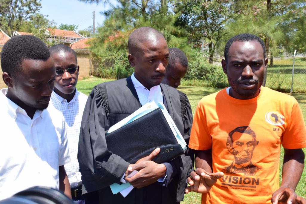 Yasin (in Orange) and Simon (in white) address the media outside Court. In the middle is their lawyer Isaac Ssemakadde.