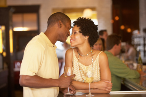 Young couple with drinks at bar in restaurant, smiling, side view