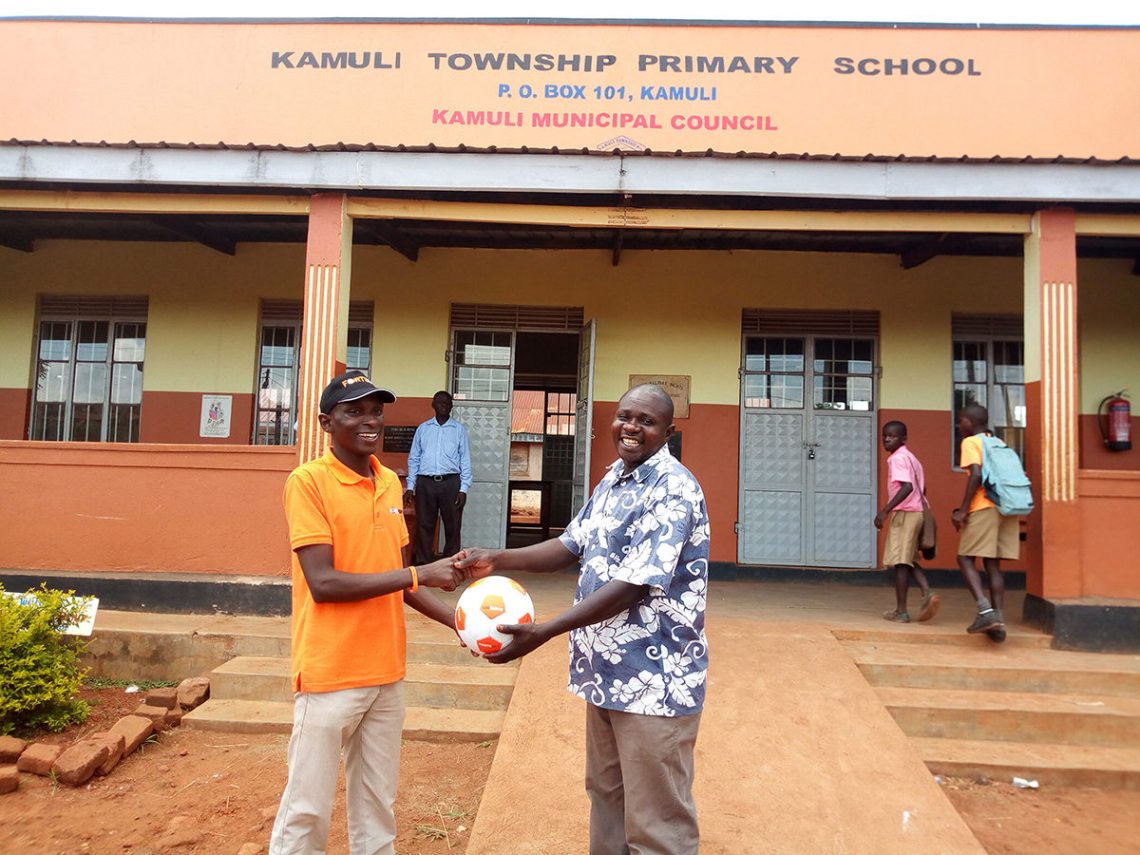 Kamuli branch operator handing over a ball to Kamuli township primary school gamesmaster